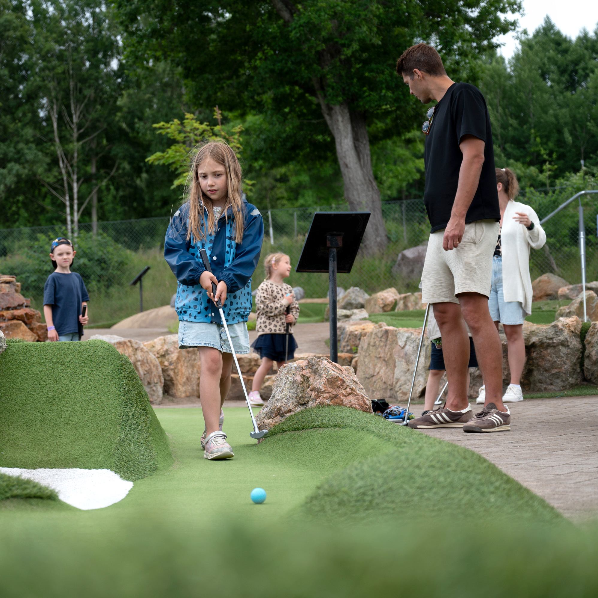 Ett barn puttar på äventyrsgolfbanan i Uddevalla medan de andra i sällskapet tittar på.